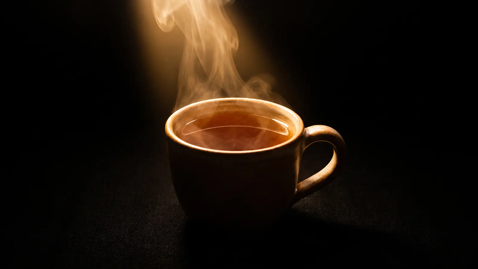 Steaming cup of Heen Bovitiya tea glowing warmly against a dark background
