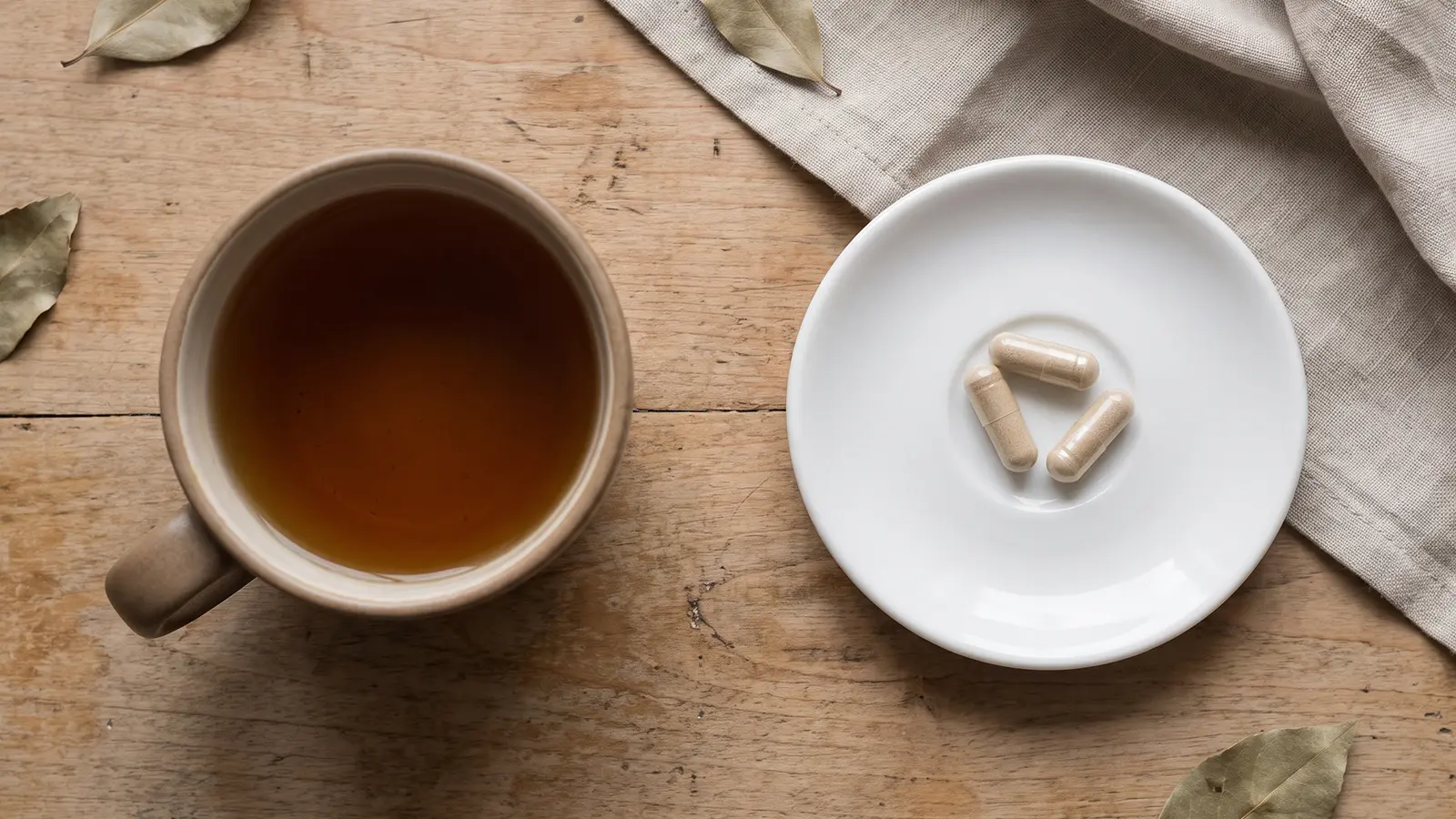 Heen Bovitiya side effects: cup of tea beside a small plate of unbranded capsules, flat lay